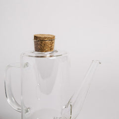 Aceitera de vidrio cilíndrica con base de corcho.